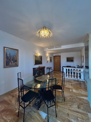 A dining area with a glass table, black chairs, a chandelier, and a painting on the wall.
