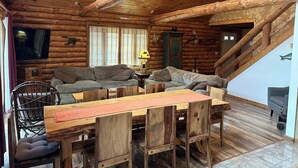 Interior de cabana de madeira com mesa e cadeiras de jantar, um sofá e uma televisão.