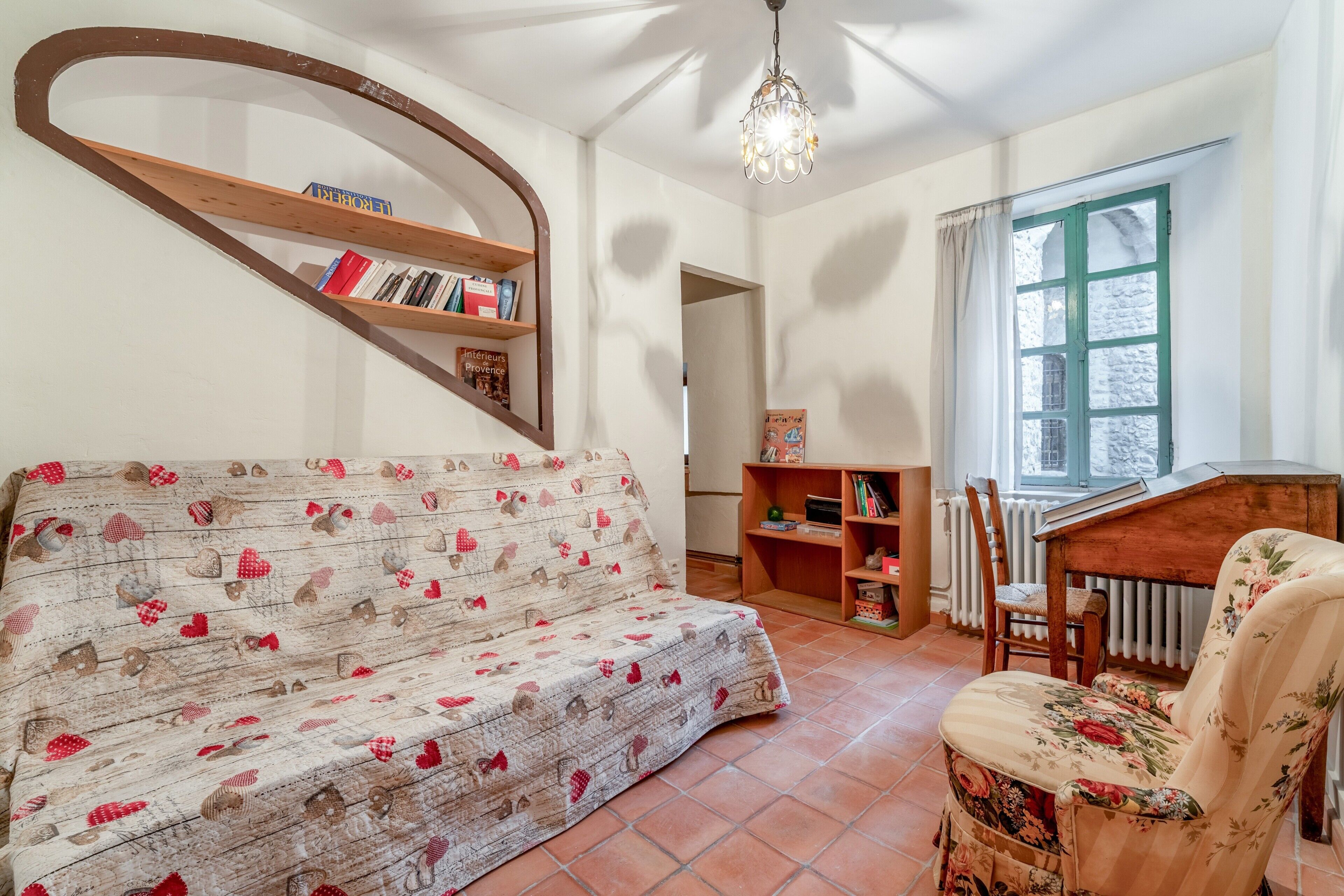 Een gezellige kamer met een bank, een stoel, een boekenkast, een radiator en een raam met gordijnen.