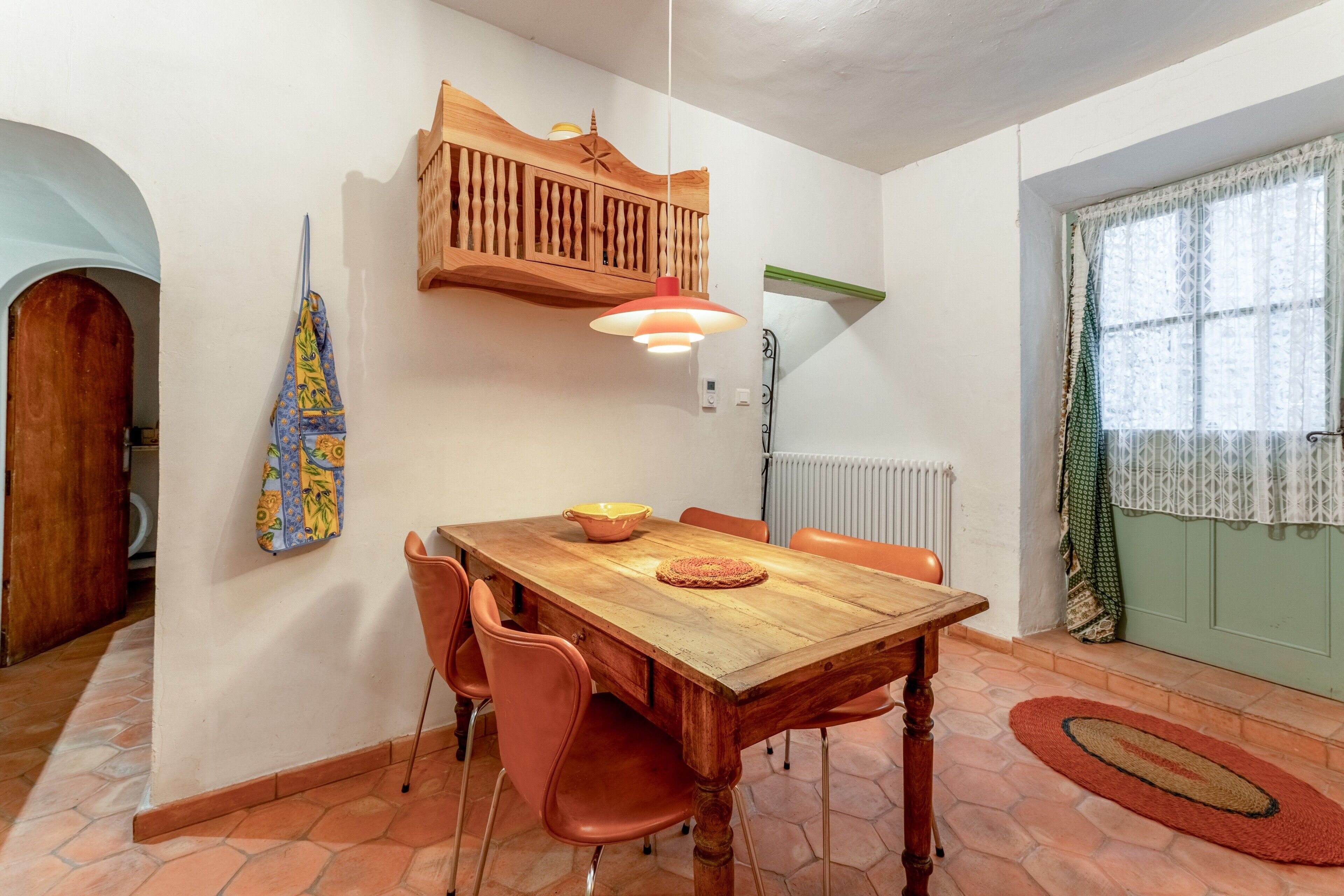 A dining area with a wooden table, orange chairs, a hanging light fixture, and a patterned towel.