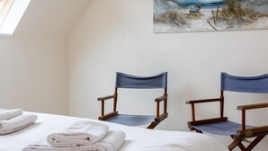 A room with a bed, two folding chairs, and a painting of a beach scene. - Apartment 'Vue Mer By Madame Est Servie' with Sea View and Balcony (Trébeurden)