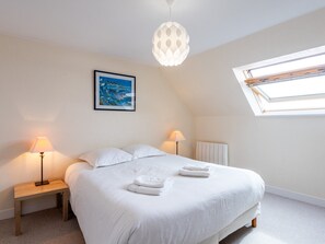 A bedroom with a bed, two bedside lamps, a picture on the wall, a window, and a ceiling light fixture.