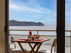 Un balcón con una mesa dispuesta para dos personas, con vistas a la costa y una montaña al fondo.