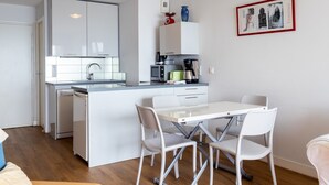 A modern kitchen with white cabinets, a central island, and a dining area with white chairs. - Apartment 'Vue Mer By Madame Est Servie' with Sea View and Balcony (Trébeurden)