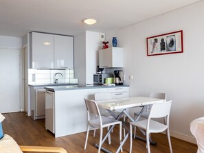 A modern kitchen with white cabinets, a central island, and a dining area with white chairs.