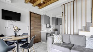 A modern living room with a grey sofa, a dining table with chairs, a TV mounted on the wall, and a kitchen area with grey cabinets. - Apartment 'Oceanida' with Sea View, Wi-Fi and Air Conditioning (Nikiana)