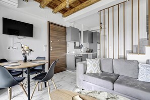 Una sala de estar moderna con un sofá gris, una mesa de comedor con sillas, un televisor montado en la pared y una zona de cocina con armarios grises.