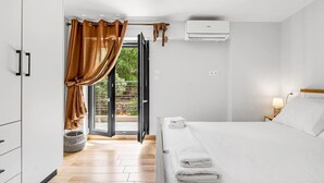 A hotel room with a bed, a nightstand, an air conditioning unit, a window with curtains, and a view of greenery outside. - Apartment 'Oceanida' with Sea View, Wi-Fi and Air Conditioning (Nikiana)