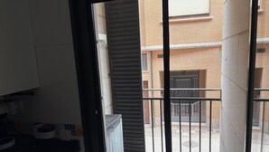 Une cuisine avec un plan de travail noir, un meuble blanc et une fenêtre donnant sur un bâtiment doté d’une grille en métal.
