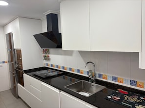 Una cocina con armarios blancos, un lavamanos de acero inoxidable, una encimera negra y un salpicadero con baldosas de colores.
