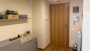 Un couloir avec une porte en bois, un radiateur, un thermostat et une étagère ornée d’objets décoratifs.