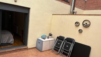 A room with a sliding door, a small cabinet, two black chairs, and a wall-mounted shelf with decorative items.