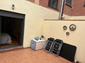 Una habitación con puerta corredera, un mueble pequeño, dos sillas negras y una estantería de pared con objetos decorativos.