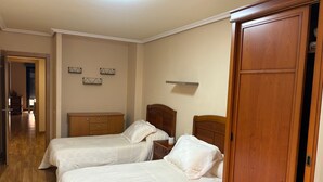 Une chambre d’hôtel avec deux lits, des têtes de lit en bois, une armoire et un couloir menant à une autre pièce.