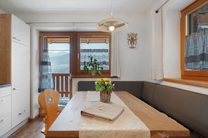 Un espace repas comprenant une table, des chaises, un banc, un livre, une plante et une vue sur les montagnes par une fenêtre.