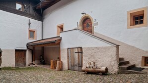 A rustic building with a cobblestone courtyard, wooden door, and a small staircase leading to an upper level. - Apartment 'Dorf' with Mountain View, Shared Garden and Wi-Fi (Castelrotto)