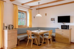 Una habitación acogedora con una mesa de madera, asientos tipo banco, un microondas, un televisor y una ventana con cortinas.