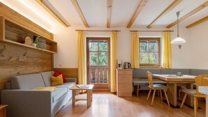 A cozy room with a sofa, a dining table with chairs, a wooden shelf, and a window with curtains. - Apartment 'Dorf' with Mountain View, Shared Garden and Wi-Fi (Castelrotto)
