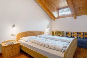 A bedroom with a wooden bed, a nightstand, a small table, a sofa, and a skylight.
