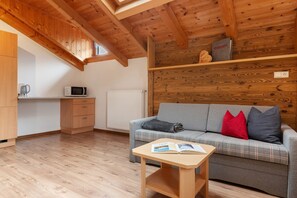 A cozy room with a wooden ceiling, a plaid sofa, a small table with a book, a microwave, and a radiator.