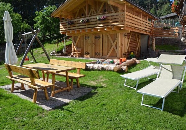 A wooden cabin with a picnic table and lounge chairs in a grassy yard.