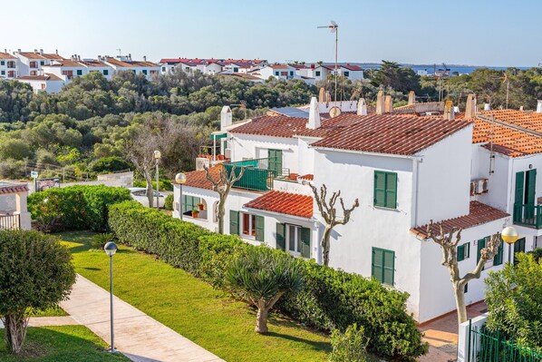 Una zona residencial con edificios blancos, tejados de tejas rojas, contraventanas verdes y una vista despejada del mar al fondo.
