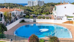 Una piscina con una sección circular, rodeada por una cerca, con edificios y follaje al fondo.