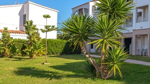 Un edificio de fachada blanca, tejado de tejas rojas y un jardín cuidado con palmeras y arbustos.