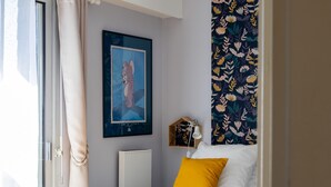 A bedroom with a bed, a window with curtains, a framed picture on the wall, and a wall-mounted lamp. - Apartment 'Ty Fox By Madame Est Servie' with Sea View and Balcony (Perros-Guirec)