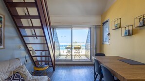 A room with a wooden staircase, a bed, a dining table with chairs, a balcony with a table and chairs, and a view of the sea. - Apartment 'Ty Fox By Madame Est Servie' with Sea View and Balcony (Perros-Guirec)