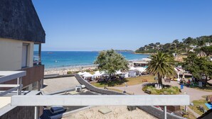 A coastal view with a beach, palm trees, and a building with a sloped roof. - Apartment 'Ty Fox By Madame Est Servie' with Sea View and Balcony (Perros-Guirec)