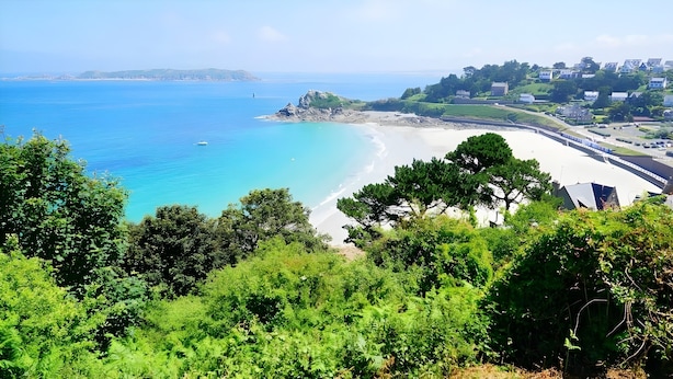 A coastal landscape with a beach, dense greenery, and a distant town. - Apartment 'Ty Fox By Madame Est Servie' with Sea View and Balcony (Perros-Guirec)