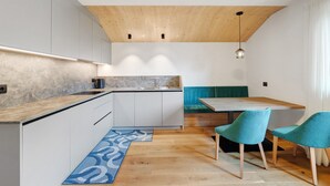 A modern kitchen with a wooden ceiling, a dining area with teal chairs, and a kitchen island. - Apartment 'Lü Da Plazores Codà' with Mountain View, Shared Garden & Wi-Fi (Marebbe)
