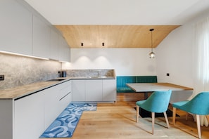 Una cucina moderna con soffitto in legno, un'area pranzo con sedie color petrolio e un'isola per la preparazione dei cibi.
