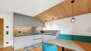 A modern kitchen with white cabinets, a wooden ceiling, and a dining area with teal chairs. - Apartment 'Lü Da Plazores Codà' with Mountain View, Shared Garden & Wi-Fi (Marebbe)