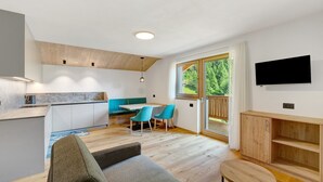 A modern kitchen with a dining area, a sofa, and a TV mounted on the wall. - Apartment 'Lü Da Plazores Codà' with Mountain View, Shared Garden & Wi-Fi (Marebbe)