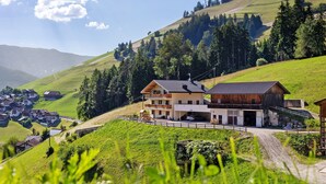 A multi-story building with a sloped roof, a garage, and a paved driveway. - Apartment 'Lü Da Plazores Codà' with Mountain View, Shared Garden & Wi-Fi (Marebbe)