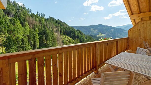 A wooden balcony with a table and chairs, overlooking a forested mountain landscape. - Apartment 'Lü Da Plazores Codà' with Mountain View, Shared Garden & Wi-Fi (Marebbe)