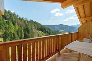 Un balcon en bois avec une table et des chaises, offrant une vue sur un paysage montagneux boisé.
