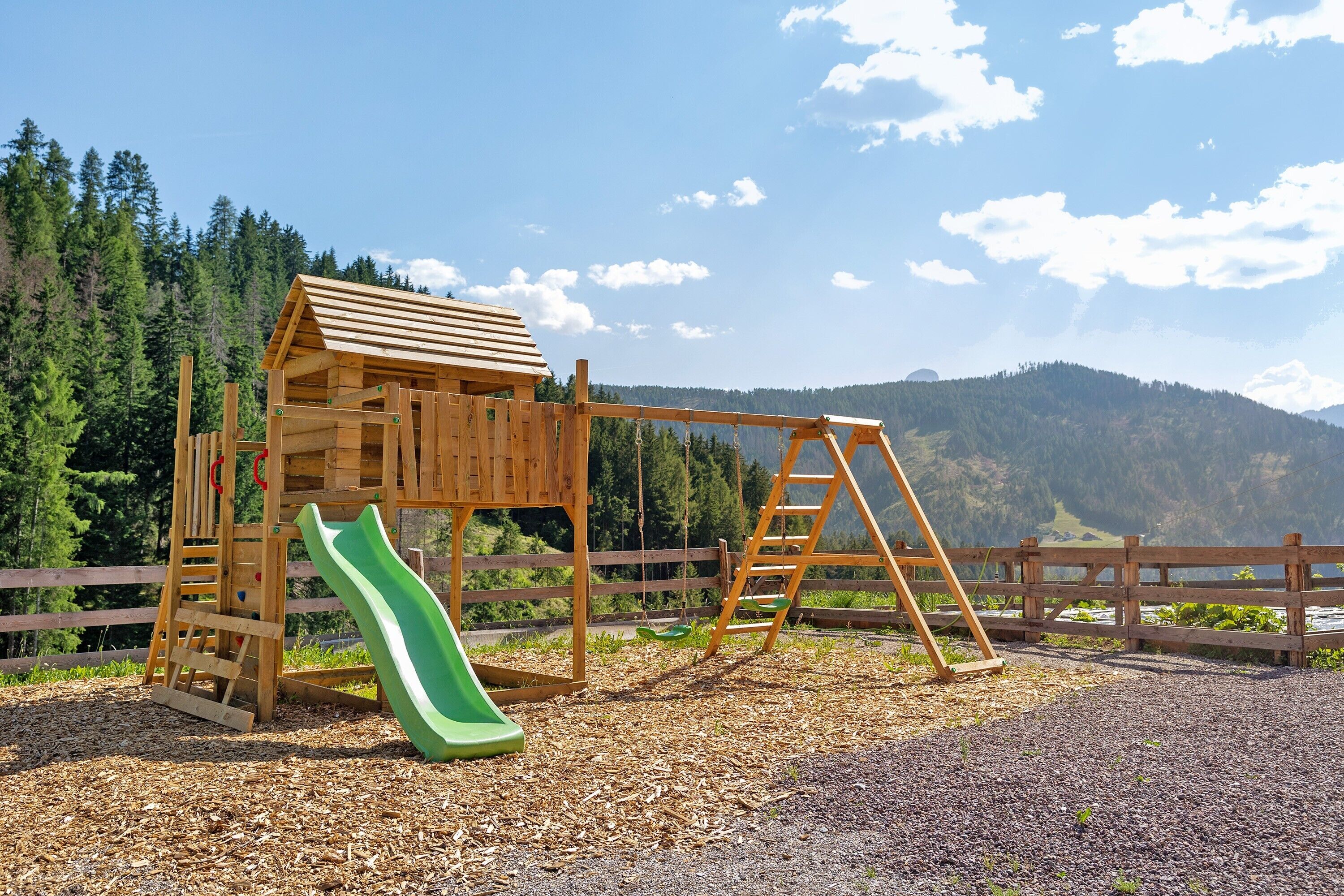 A wooden play structure with a slide, a swing set, and a ladder.
