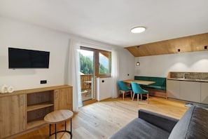A modern interior with a wooden dining table, green sofa, and a TV mounted on the wall. - Apartment 'Lü Da Plazores Falc' with Mountain View, Shared Garden and Wi-Fi (Marebbe)