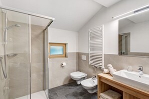 A modern bathroom with a glass shower enclosure, a toilet, bidet, and a sink with a mirror above.