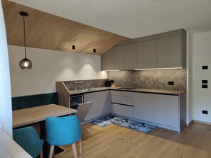 A modern kitchen with a wooden ceiling, built-in cabinets, a dining area with a table and chairs, and a small island with a sink. - Apartment 'Lü Da Plazores Falc' with Mountain View, Shared Garden and Wi-Fi (Marebbe)