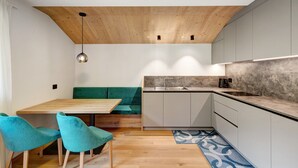 Una cucina moderna con soffitto in legno, mobili grigi, un tavolo da pranzo in legno, sedie color petrolio e un tappeto con motivi blu.