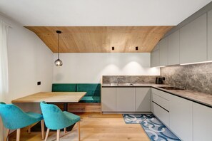 A modern kitchen with wooden ceiling, grey cabinets, a wooden dining table, teal chairs, and a blue patterned rug. - Apartment 'Lü Da Plazores Falc' with Mountain View, Shared Garden and Wi-Fi (Marebbe)