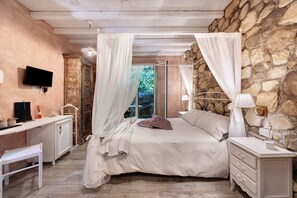 A bedroom with a stone wall, a bed with a canopy, a desk, and a television.