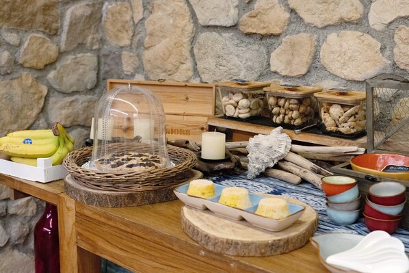 A wooden table with a stone wall background, containing a variety of food items and kitchenware.