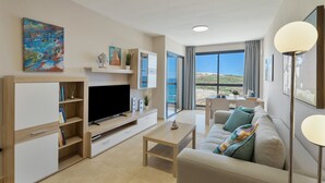 A modern living room with a flat-screen TV, a sofa, a coffee table, and a large window offering a view of the sea. - Vacation 'Maresía' with Sea View, Private Terrace and Wi-Fi (Los Abrigos)