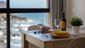 A dining table with a bottle of wine, glasses, and bowls, overlooking a rocky coastline. - Vacation 'Maresía' with Sea View, Private Terrace and Wi-Fi (Los Abrigos)