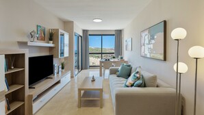 A modern living room with a flat-screen TV, a sofa, a coffee table, and a dining area with a view. - Vacation 'Maresía' with Sea View, Private Terrace and Wi-Fi (Los Abrigos)